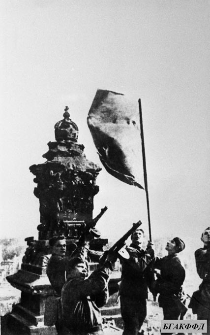 Пятеро советских солдат водружают знамя над зданием рейхстага и салютуют из автоматов в честь Победы